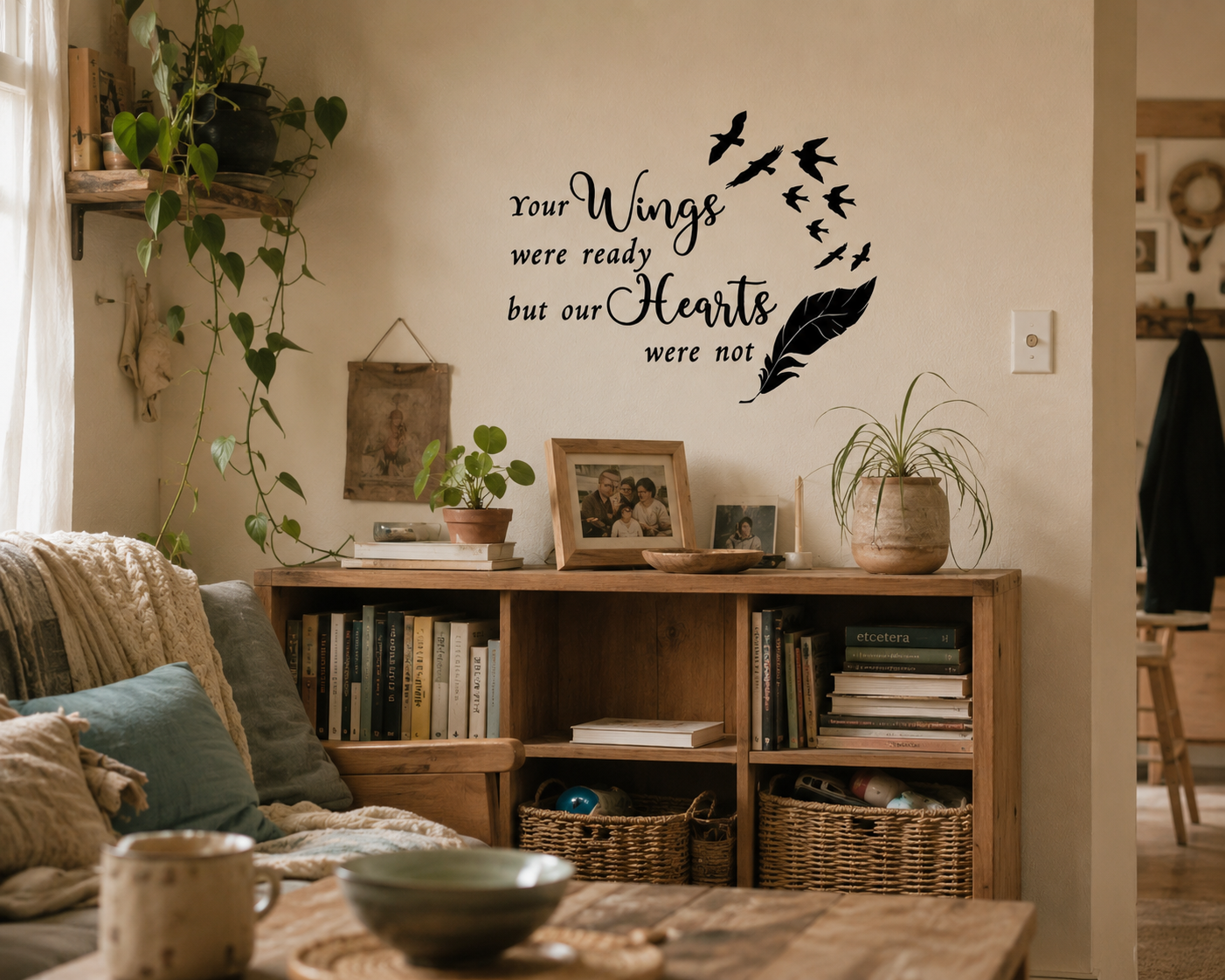 Memorial wall decal reading “Your Wings Were Ready But Our Hearts Were Not” displayed above a wooden shelf in a warm lived-in neutral home with books, plants and family decor.