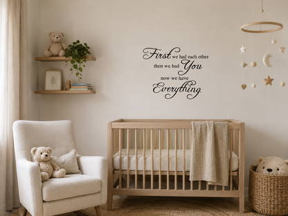 Black removable vinyl wall decal reading “First we had each other then we had you now we have everything” displayed above a wooden cot in a calm neutral nursery.