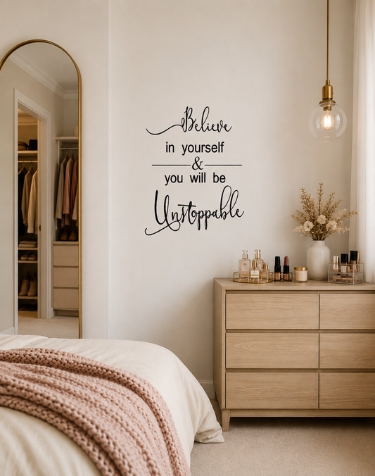 Believe in Yourself and You Will Be Unstoppable removable black vinyl wall decal displayed in a modern neutral bedroom beside a mirror and wooden dresser.