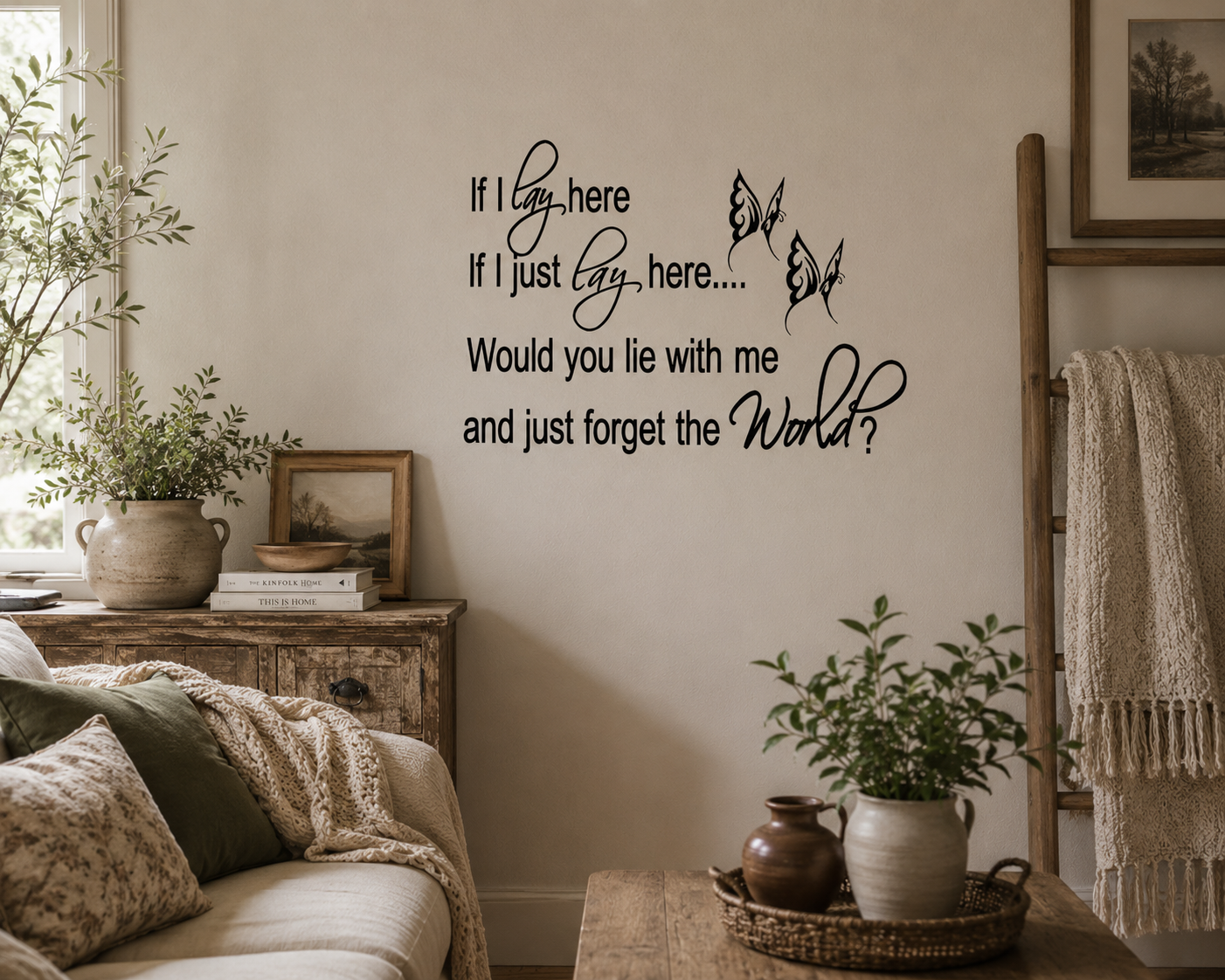Living room with a wall decal, plants, and a couch. Black romantic quote wall decal with butterfly details displayed in a cosy neutral-toned living room with rustic décor and soft natural lighting.