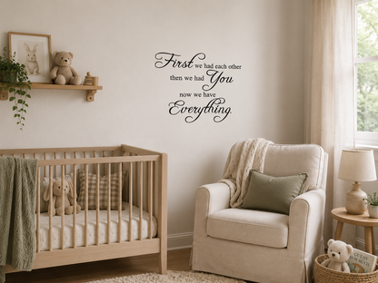 Black removable vinyl wall decal reading “First we had each other then we had you now we have everything” displayed above a wooden cot in a calm neutral nursery.