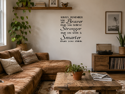 A beautiful modern living room featuring a motivational wall decal reading “Always Remember You Are Braver Than You Believe, Stronger Than You Seem & Smarter Than You Think” displayed above a fireplace with neutral décor and indoor plants.