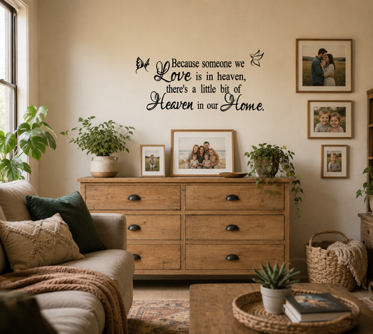 Memorial wall decal featuring the quote “Because someone we love is in heaven” displayed above wooden drawers surrounded by family photo frames in a warm lounge room.